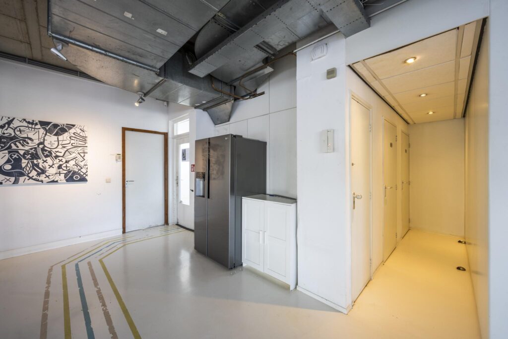 Moderne gemeenschappelijke ruimte aan de Anthony Fokkerweg met een metalen plafond, kunst aan de muur, een grote koelkast en meerdere deuren naar aparte ruimtes.